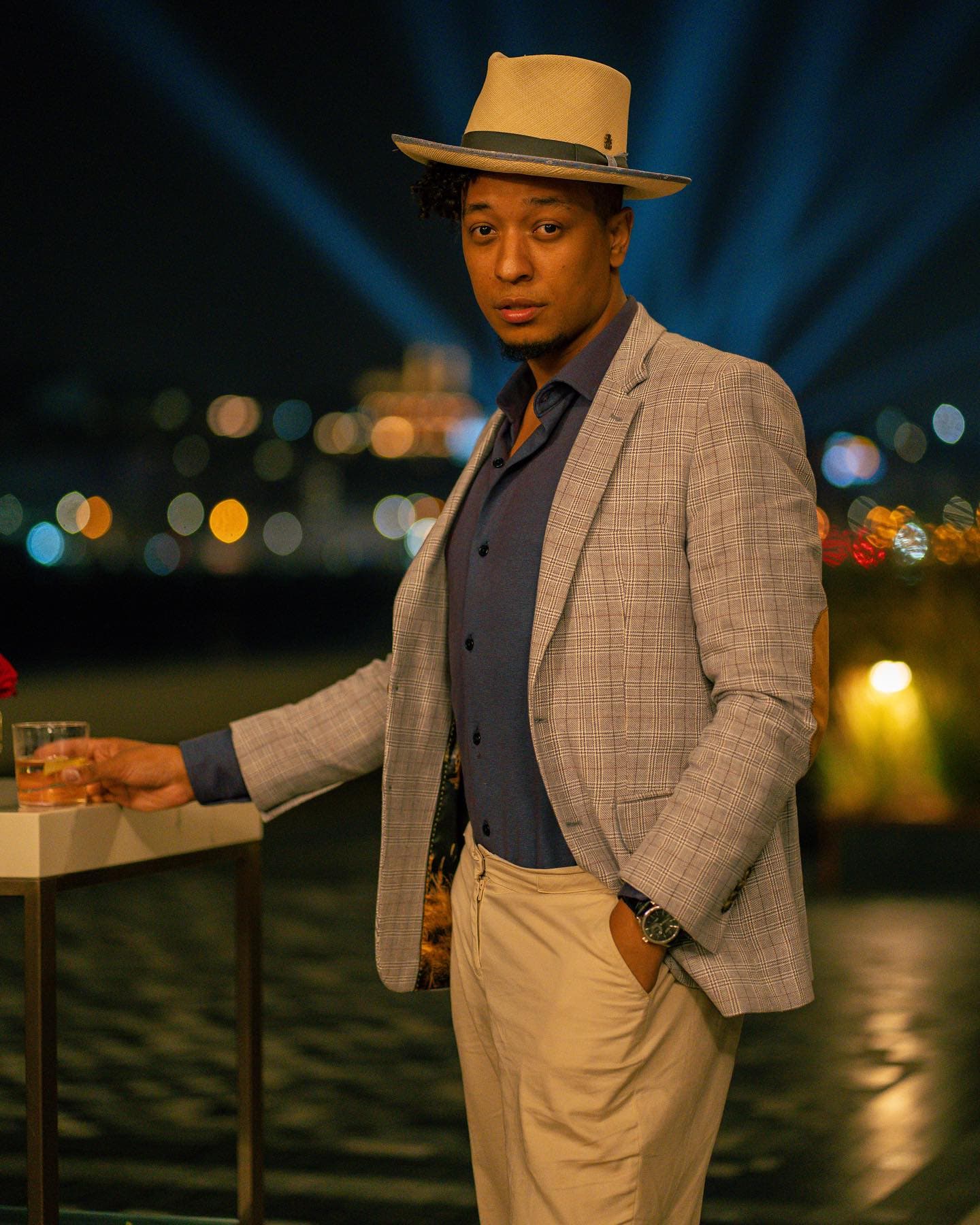 Cliente de blazer xadrez e chapéu em evento noturno